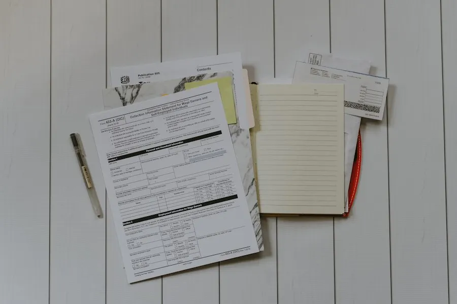 Printed forms, envelopes, a notebook and a pen spread out on a white wooden surface