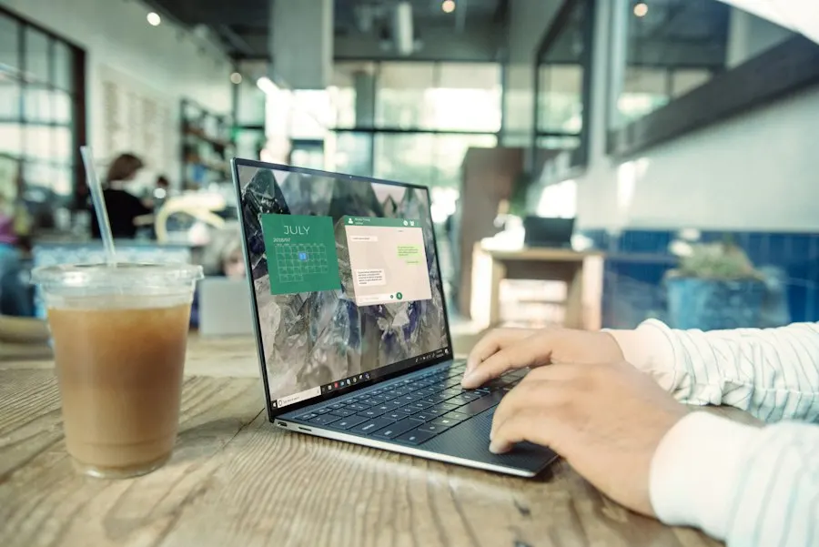 Hands typing on a laptop on a wooden café table beside an iced coffee
