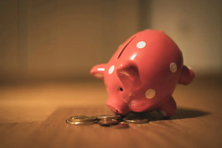 A red polka-dot piggy bank on a wooden table beside a few scattered coins