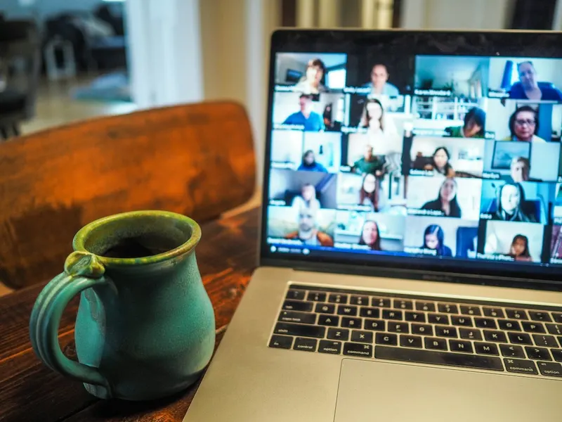 A laptop showing a video call with a grid of many participants, next to a green ceramic mug